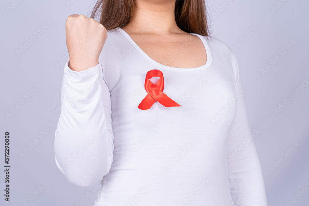Red AIDS awareness ribbon on woman chest and raise her hand to fight them on grey background. World Aids Day, Healthcare and medical concept. Red AIDS awareness ribbon on woman chest and raise her hand to fight them on grey background. World Aids Day, Healthcare and medical concept.