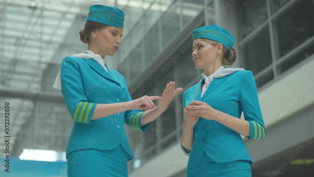 Excited beautiful stewardess explaining work of new technical device to young colleague in airport. Angle bottom view of Caucasian women talking before departure. Portrait of happy flight attendants. Excited beautiful stewardess explaining work of new technical device to young colleague in airport. Angle bottom view of Caucasian women talking before departure. Portrait of happy flight attendants.