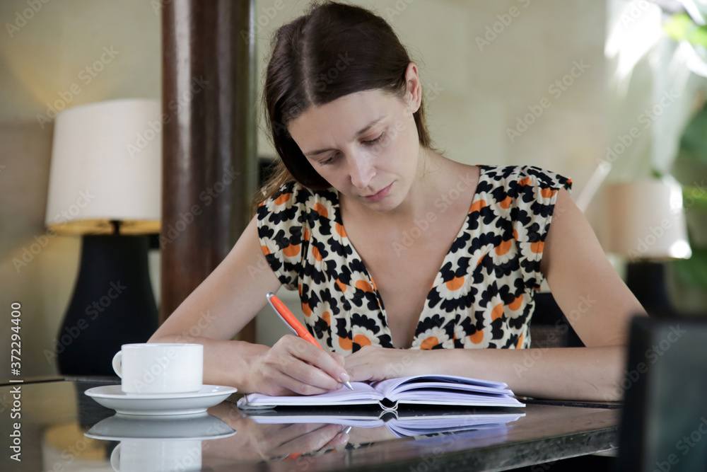 Young thoughtful woman at home writing in journal. Female writer with pen and notebook sitting at the table. Education, freelance work or creative process concept. Young thoughtful woman at home writing in journal. Female writer with pen and notebook sitting at the table. Education, freelance work or creative process concept.