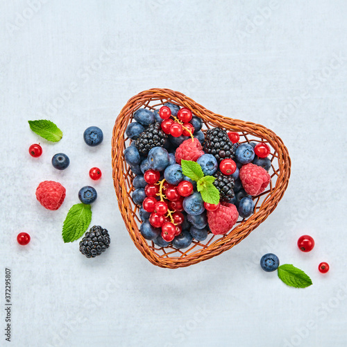 Blueberry, raspberry, blackberry, redcurrant in heart basket. Fresh blueberry, berries mix on marble. Red raspberry, mint creative composition. Colorful concept, top view.