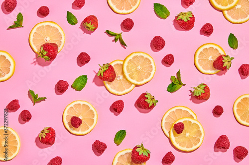 Red raspberry, strawberry, lemon colorful pattern on pink background. Fresh berry closeup, strawberry wallpaper, top view. Lemonade creative concept, fashionable trendy summer beverage, flat lay