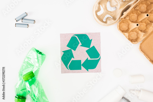 Top view of plastic bottles, cardboard egg tray and accumulators near card with recycle sing on white background, ecology concept