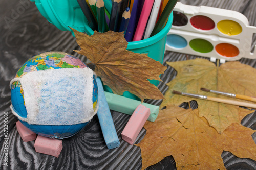 Globe with medical mask. Nearby watercolors, crayons and pencils. Academic year during the epidemic.