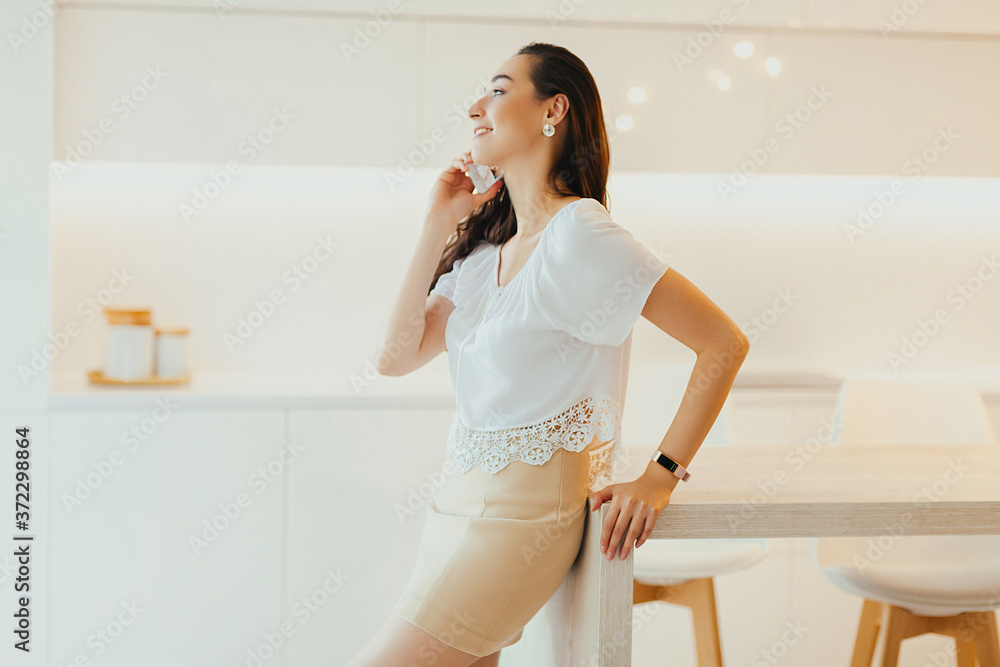 Happy young beautiful woman speaks on phone in minimalistic light kitchen Happy young beautiful woman speaks on phone in minimalistic light kitchen