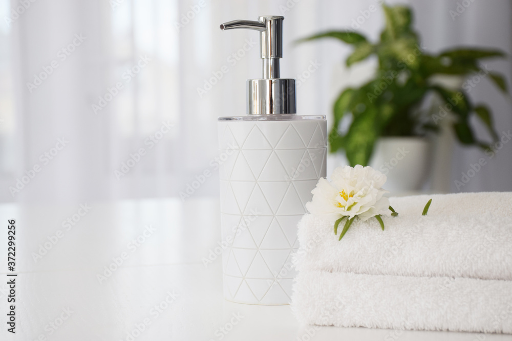 Fresh white towels folded on white table, white flower and liquid container with green leaves of house plant and tulle window on background. Spa and wellness or massage salon concept. Copy space. Fresh white towels folded on white table, white flower and liquid container with green leaves of house plant and tulle window on background. Spa and wellness or massage salon concept. Copy space.