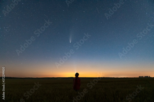 Fototapeta Naklejka Na Ścianę i Meble -  Silhouette of a man standing at night in a field outside the city. Starry night sky with comet Neowise C/2020 F3