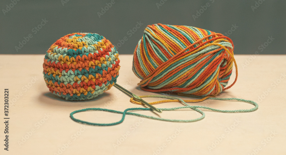 Skein of multi colored cotton yarn with a crochet hook and a completed amigurumi ball Skein of multi colored cotton yarn with a crochet hook and a completed amigurumi ball
