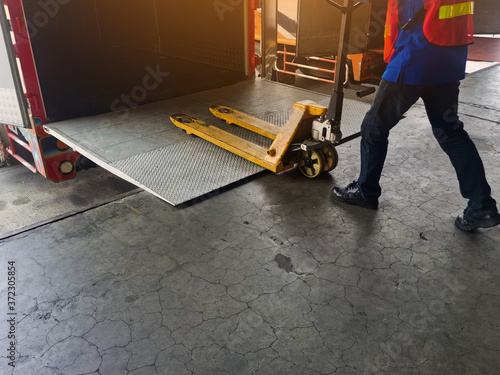 Worker driving forklift loading shipment carton boxes and goods on wooden pallet at loading dock from container truck to warehouse cargo storage in freight logistics and transportation industrial photo