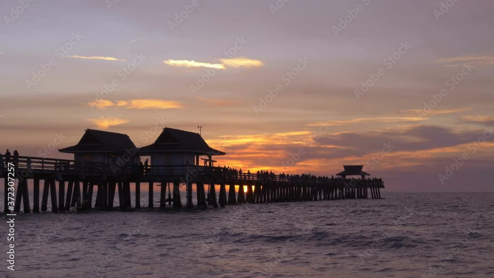SLOW MOTION: Naples Beach and Fishing Pier at Sunset, Florida. Dark silhouette of a pier over the water at sunset. Sunset over horizon and wooden pier of caribbean beach of Naples in Florida. Sunset. SLOW MOTION: Naples Beach and Fishing Pier at Sunset, Florida. Dark silhouette of a pier over the water at sunset. Sunset over horizon and wooden pier of caribbean beach of Naples in Florida. Sunset.