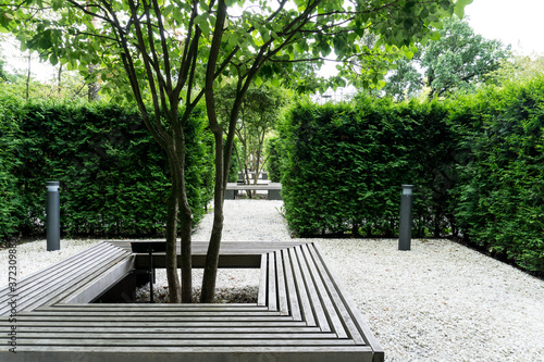 Square-shaped bench installed around the bush. The park space is divided by evergreen bushes into small cozy parts. A good place for privacy, concentration and relaxation.