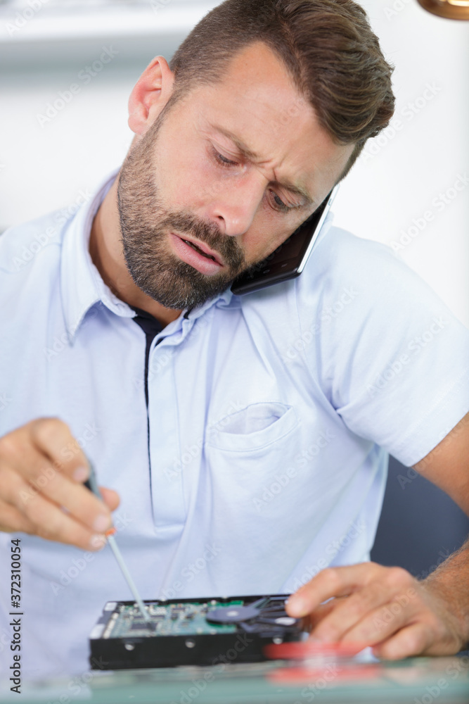 computer specialist repairing hard drive and talking on smartphone computer specialist repairing hard drive and talking on smartphone