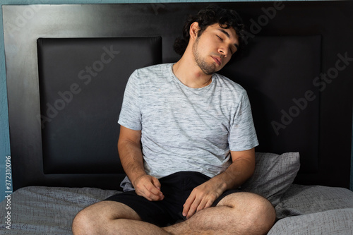 Young hispanic man with long curly hair taking a nap on a bed with gray sheets