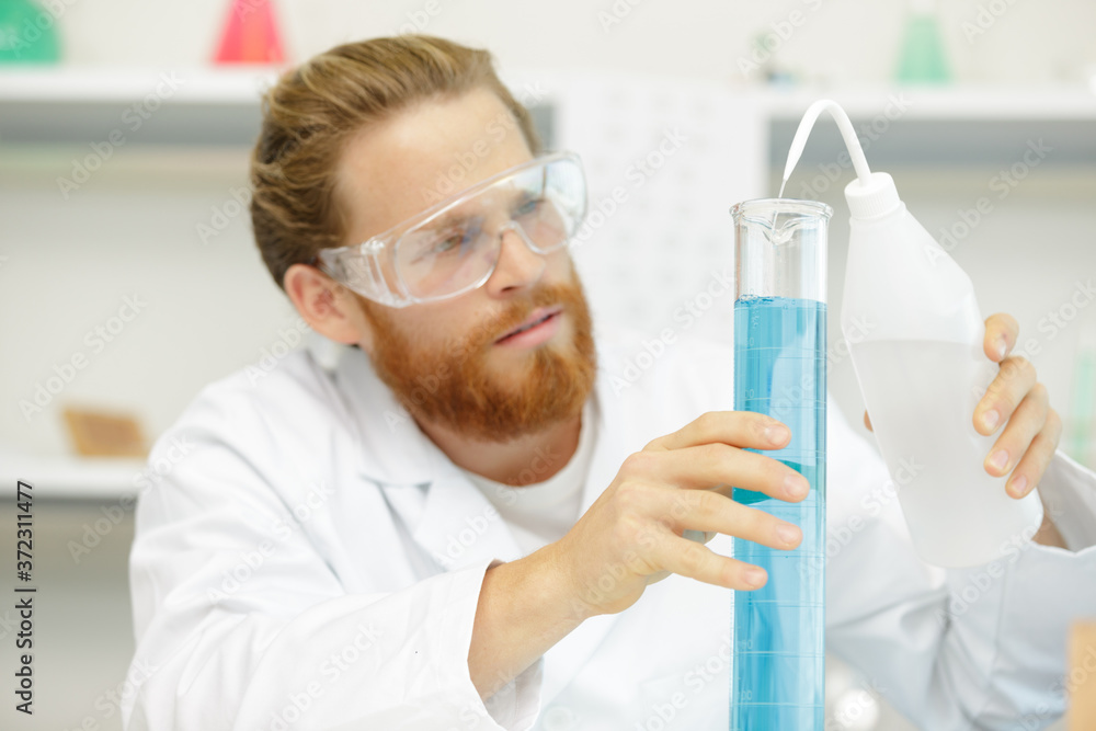 male scientist adding solution to blue liquid in flask male scientist adding solution to blue liquid in flask