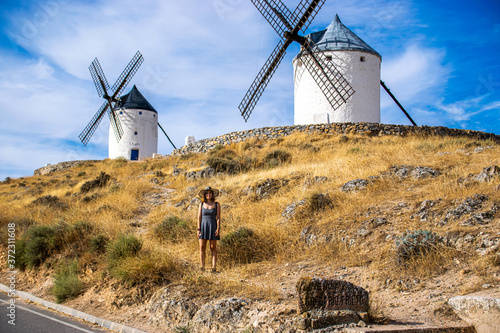 Photo of an attractive woman standing next to some beautiful and historic windmills located in Consuegra, Toledo, Spain during a sunny day of summer in a natural place.  photo