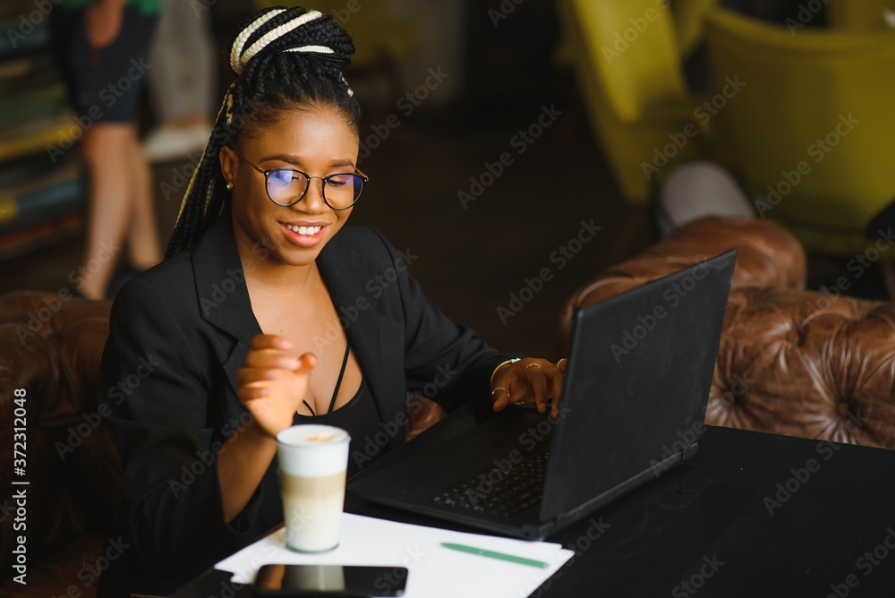 Satisfied african girl using laptop at cafe, working online, copy space