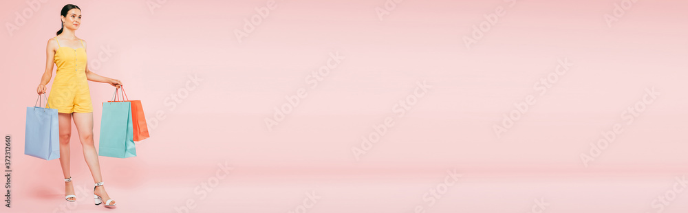 full length view of brunette young woman with shopping bags on pink, panoramic shot full length view of brunette young woman with shopping bags on pink, panoramic shot