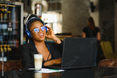 Young african american girl sitting at cafe table with laptop and looking at screen. Dark skinned freelancer concept.