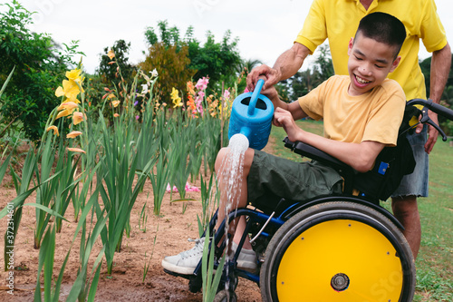 Asian special child on wheelchair and father watering the plants in flower garden,Daily activities happiness with family time in the home,Lifestyle in the education age and happy disabled kid concept. photo