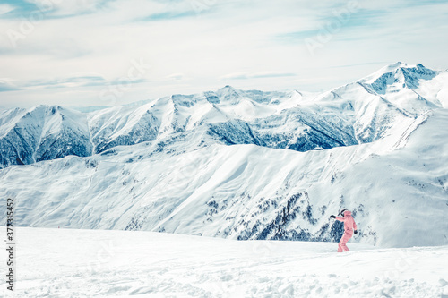 Girl in pink combinezon rides down the hill on snowboard with mountains view in the background. Skiing holidays in KAzbegi mountains.