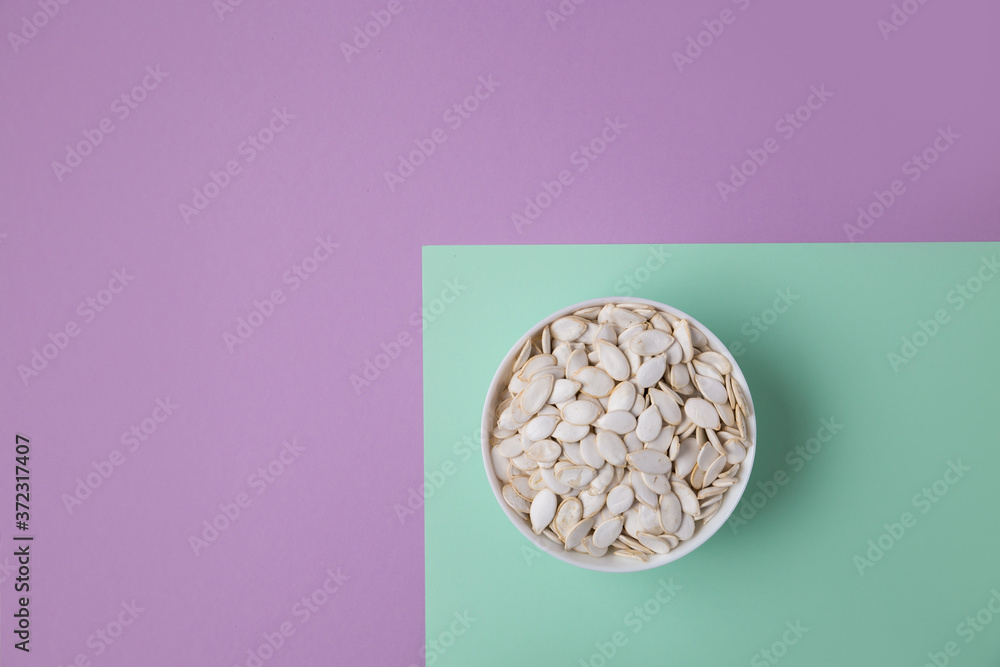 White pumpkin seeds in a bowl on a colored background. The top view image contains copy space. Concept photo White pumpkin seeds in a bowl on a colored background. The top view image contains copy space. Concept photo