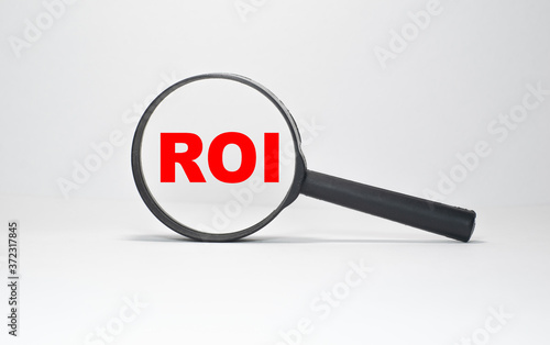 ROI RETURN ON INVESTMENT inscription in a magnifying glass on a boundless white background