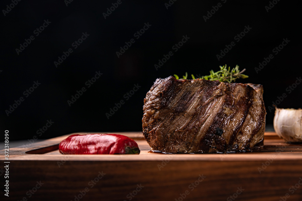 American juicy steak on the board with spices, tomato and grilled vegetables. On a black table 