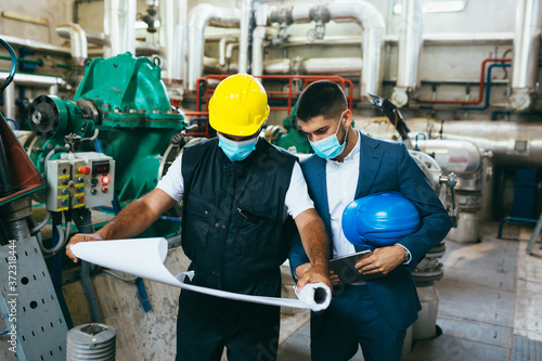 businessman and worker talking indoor in industry plant, covid protected with face masks