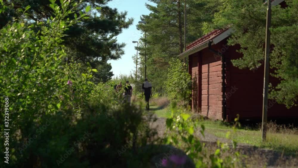 A gravel path with walking people meeting runners. Bushes to the left and a small red house to the right. No camera movements, filmed with shallow dof in real time at 4K. A gravel path with walking people meeting runners. Bushes to the left and a small red house to the right. No camera movements, filmed with shallow dof in real time at 4K.