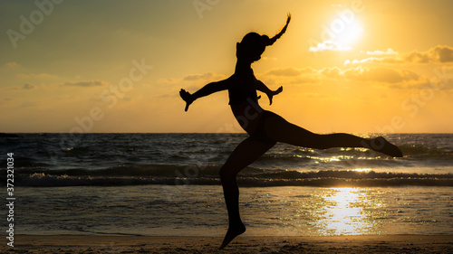 Happy woman dancing at sunset in front of the backlit Mediterranean Sea.