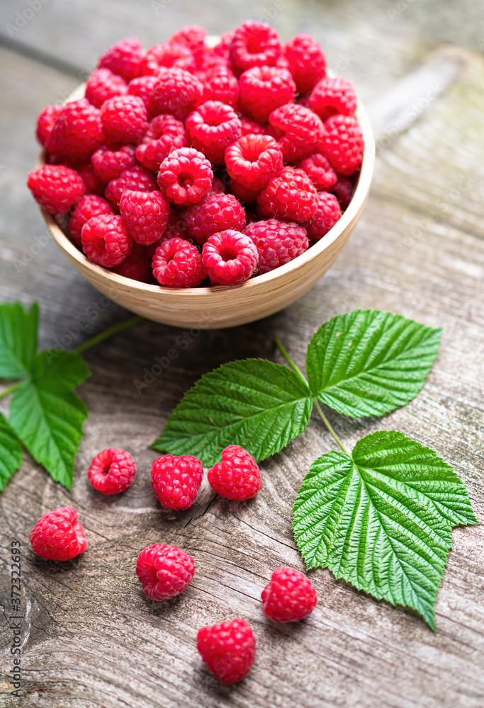 Fresh ripe red raspberries with leaves in a bowl on rustic old wooden table. Healthy organic food, summer vitamins, BIO viands, natural background. Copy space for your advertising text message Fresh ripe red raspberries with leaves in a bowl on rustic old wooden table. Healthy organic food, summer vitamins, BIO viands, natural background. Copy space for your advertising text message