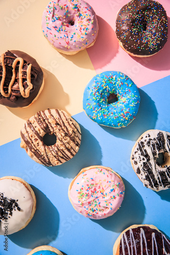Top down view of colorful donuts flat lay on top of multicolored background.