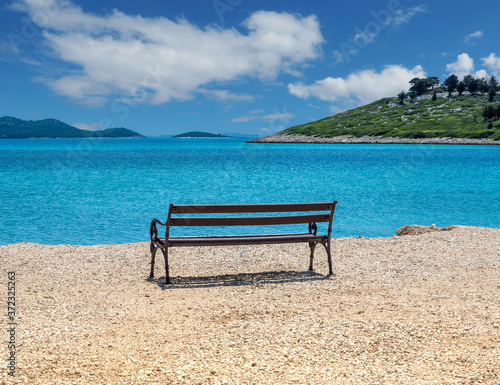 Empty wooden bench on the shore of the blue sea in calm cloudy day. © Jana Kollarova