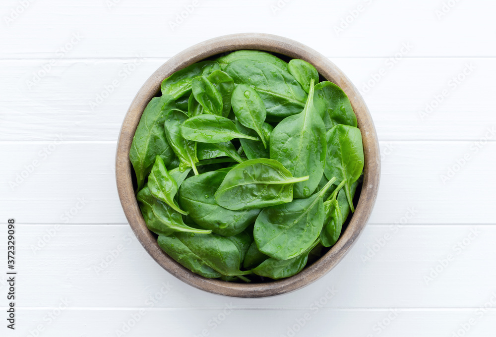 Spinach in a bowl on a white wooden background. Farm fresh spinach leaves. Spinach in a bowl on a white wooden background. Farm fresh spinach leaves.