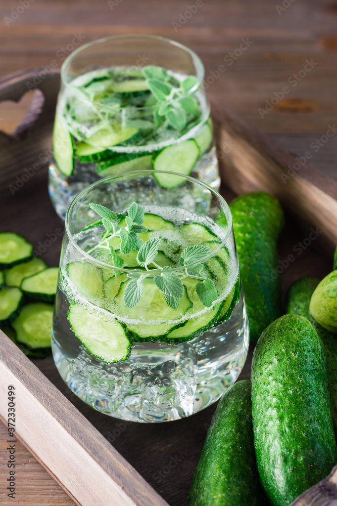 Detox drink. Water with pieces of cucumber, ice and mint leaves in transparent glasses and vegetables on a wooden tray on the table. Vertical view Detox drink. Water with pieces of cucumber, ice and mint leaves in transparent glasses and vegetables on a wooden tray on the table. Vertical view