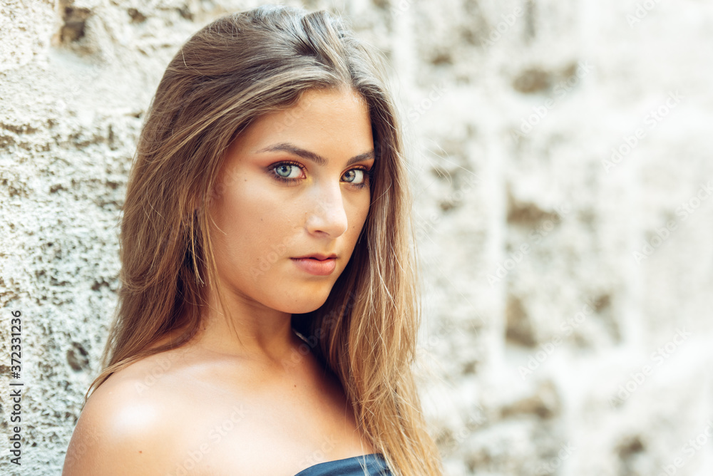 portrait of light-eyed blond young woman looking at camera, with stone wall background. portrait of light-eyed blond young woman looking at camera, with stone wall background.
