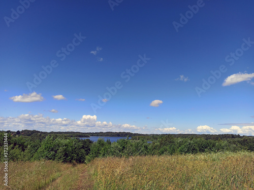 Obraz na płótnie photo of a field and a lake in the distance. sunny summer day. blue sky and green bushes. w salonie