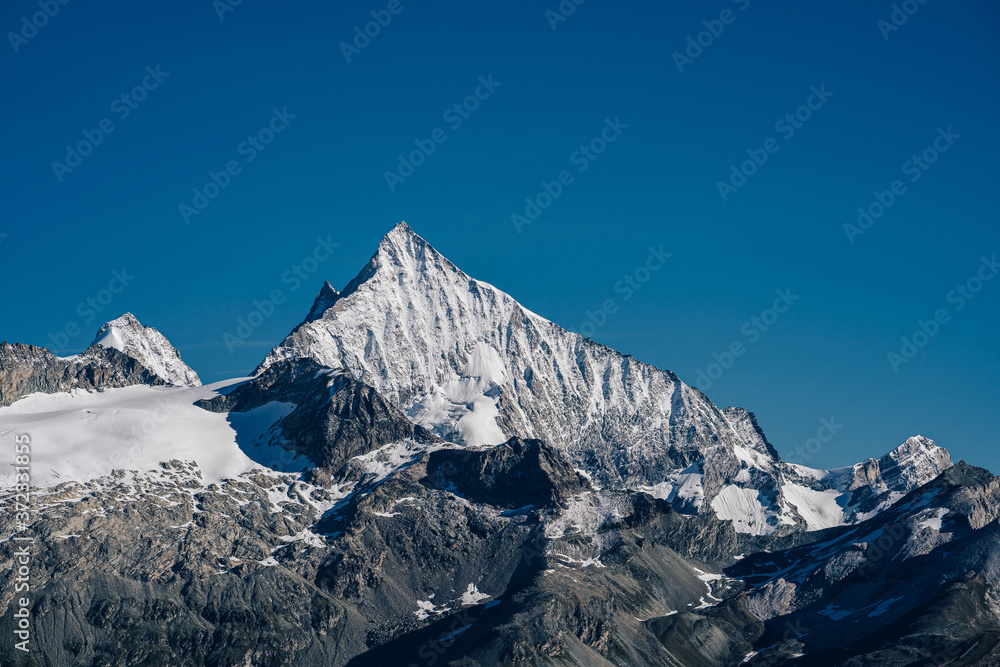 Beautiful view of a famous alpine peak Weisshorn (4506 m) in Valais, Switzerland. High and sharp, snow covered mountain of Wiesshorn under a blue sky. Alpine mountain landscape with rock, snow and ice