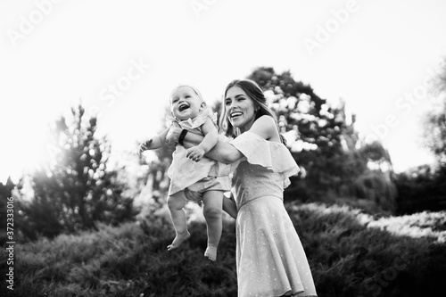 Overjoyed mother play with adorable daughter at the park, pretty woman hold baby girl in caring arms, smile, enjoy happy family moments, weekend outdoors, parenthood concept