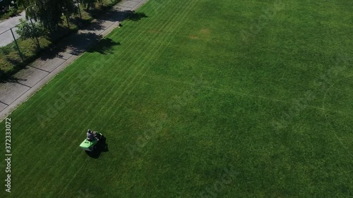 Aerial view of a man on a lawn mower mows green grass on a soccer field
