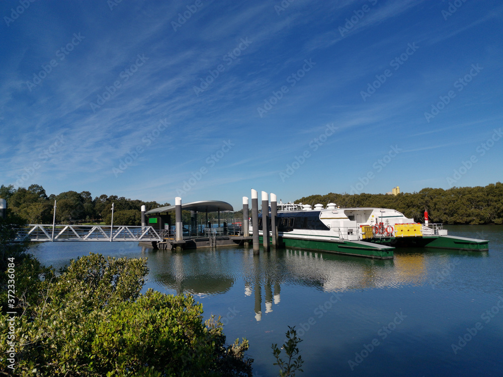 Beautiful view of a wharf with boat and reflections of wharf structure, trees and blue sky on water, Parramatta River, Rydalmere Wharf, Rydalmere, Sydney, New South Wales, Australia