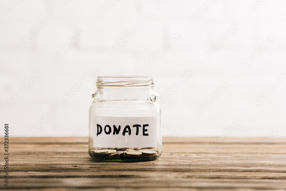 penny jar with donate lettering on wooden surface on white background penny jar with donate lettering on wooden surface on white background