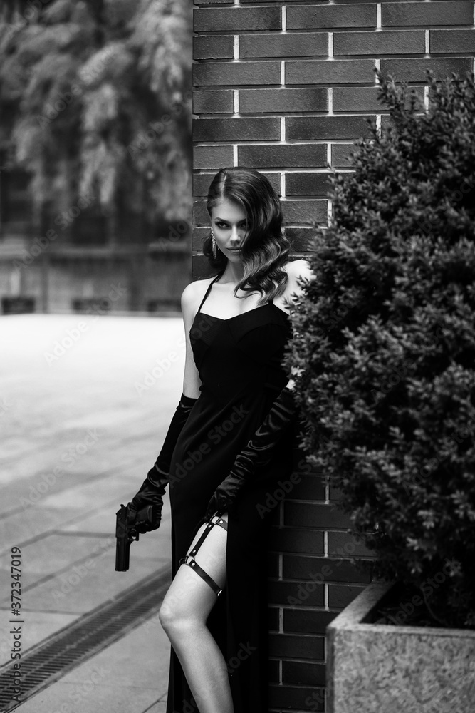 Beautiful young girl in an elegant dress. Woman holding a gun in her hands.  Fashion model