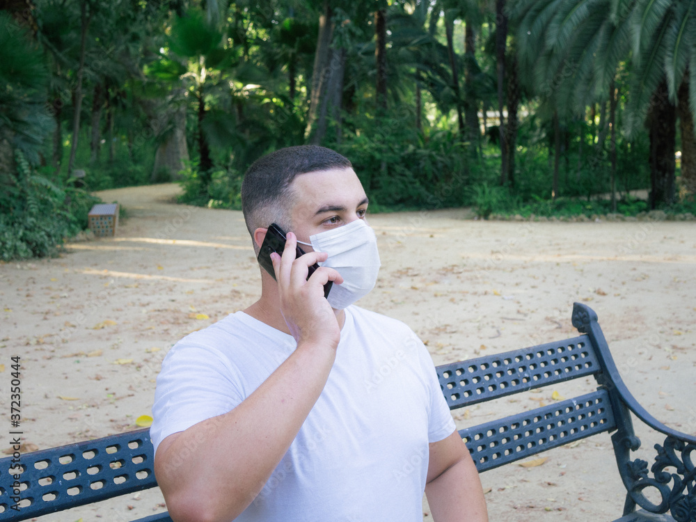 Fototapeta premium Hombre joven usando el smartphone con una mascarilla en la boca
