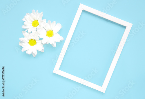 Mockup square white frame with white flowers on blue background. View top. Messege or invitation card mock-up concept. flower layut. copy space for text
