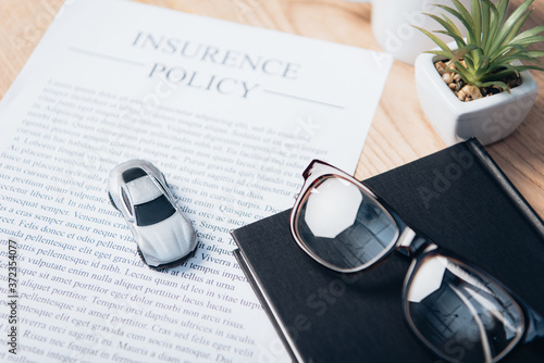 Φωτογραφία toy car on insurance policy agreement near notebook, plant and glasses
