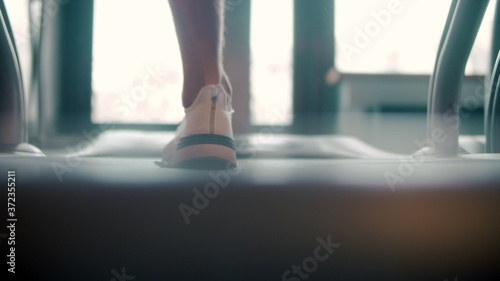 Back view on man feet running on trademill in sport club. Closeup sportsman legs