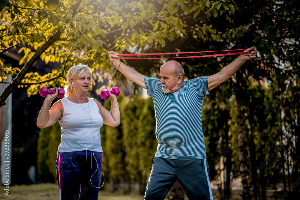 Obraz premium Healthy senior couple exercising with dumbbells and elastic band