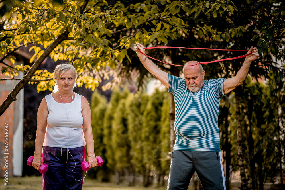 Obraz premium Healthy senior couple exercising with dumbbells and elastic band
