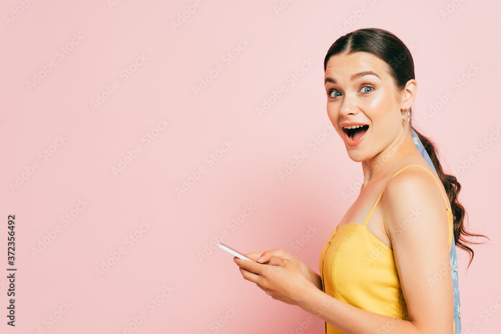 side view of surprised brunette young woman using smartphone isolated on pink side view of surprised brunette young woman using smartphone isolated on pink
