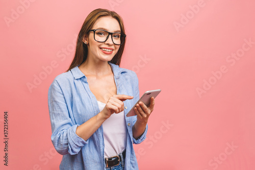 Portrait of a happy young business woman using mobile phone isolated over pink background.